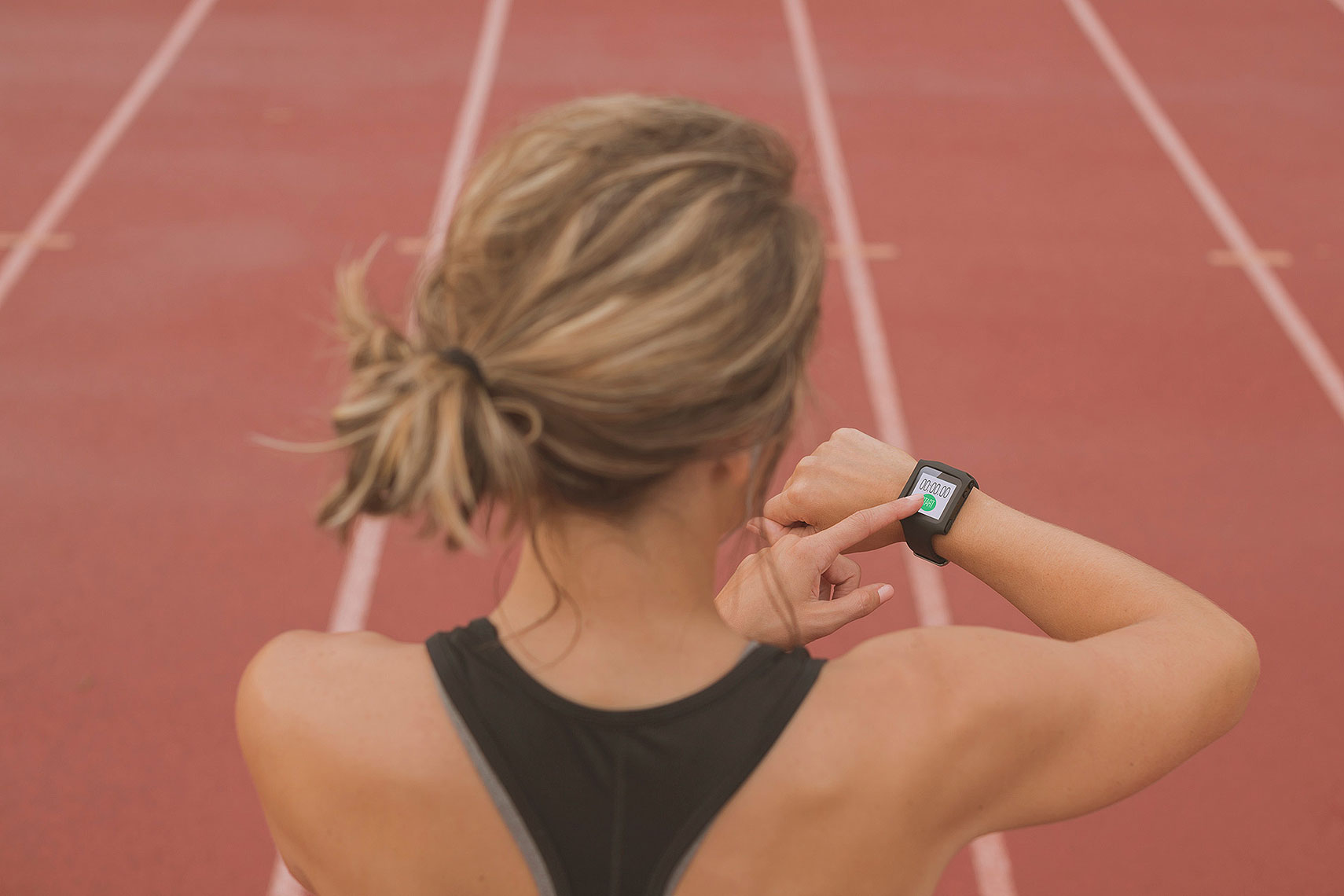 Woman setting her fitness tracker on a track. | John Fedele Lifestyle Photography