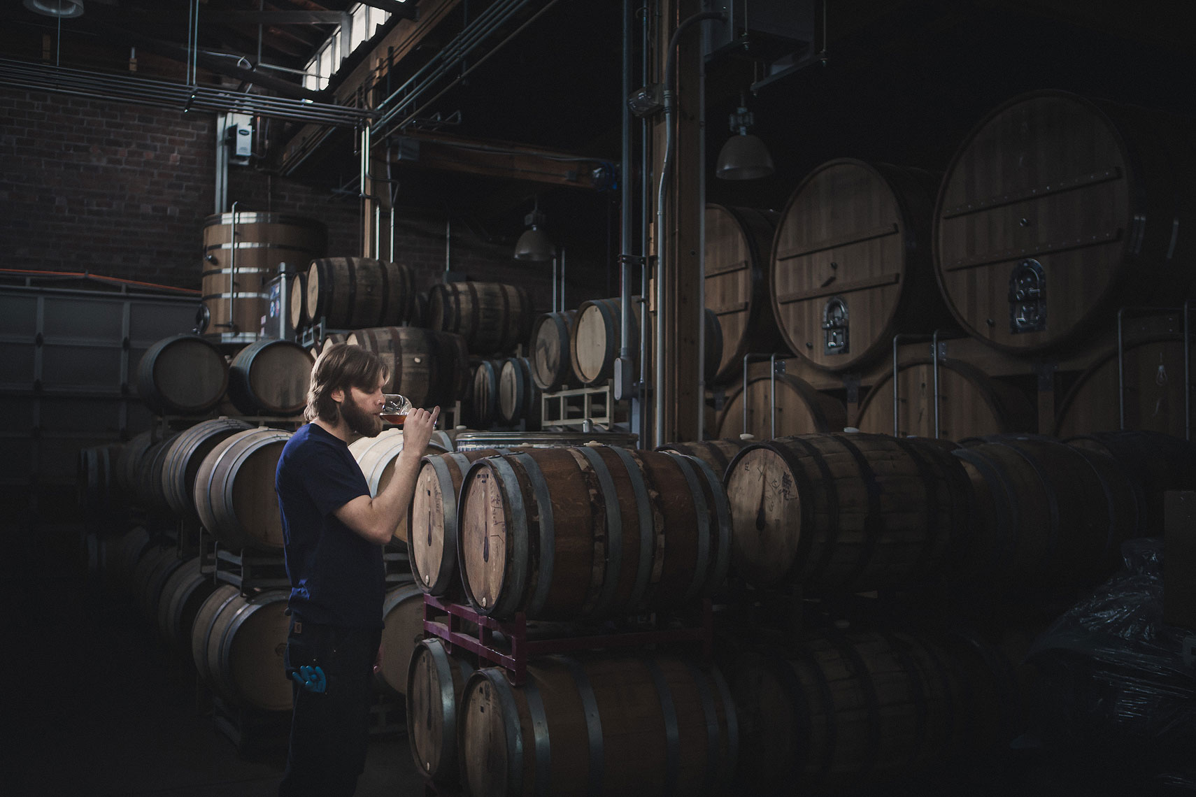 Man tasting a beer out of aging whiskey barrels in a warehouse | Side Project Brewery | John Fedele Photography 